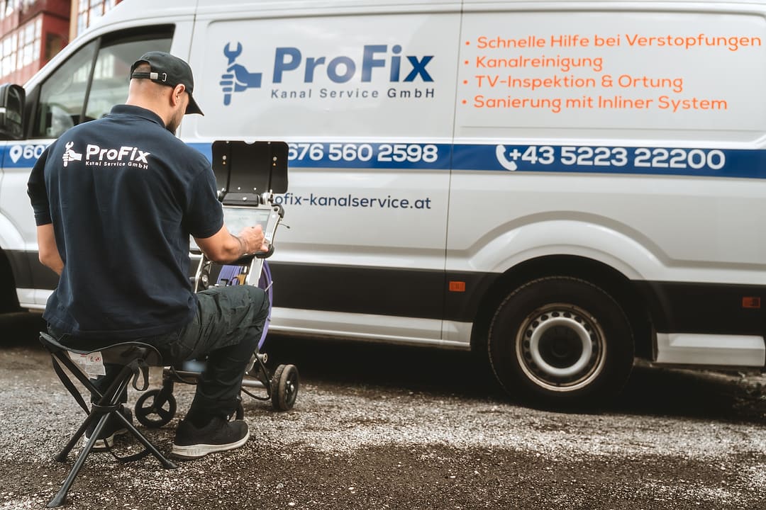 Techniker von ProFix von hinten am Kamerawagen vor dem beschrifteten Firmenwagen